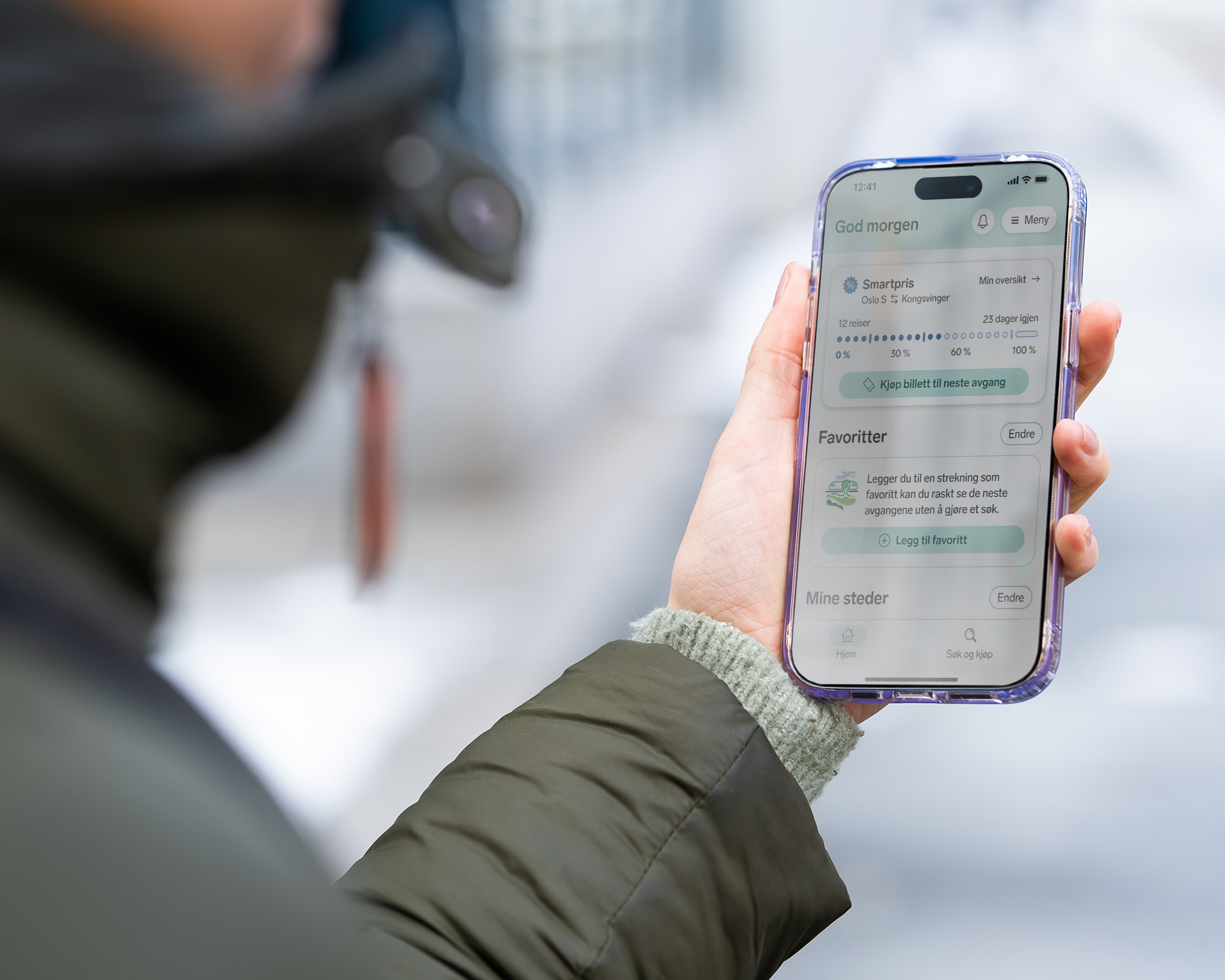 En arm med grønn boblejakke på, med en hånd som holder en mobil med Smartpris på skjermen