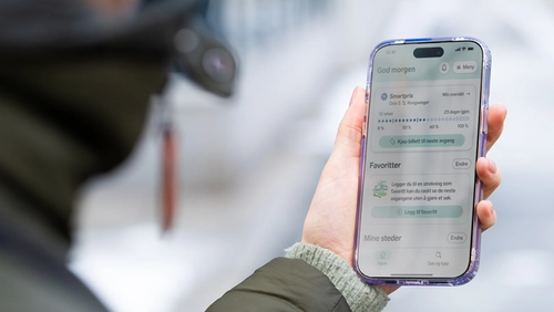 En arm med grønn boblejakke på, med en hånd som holder en mobil med Smartpris på skjermen