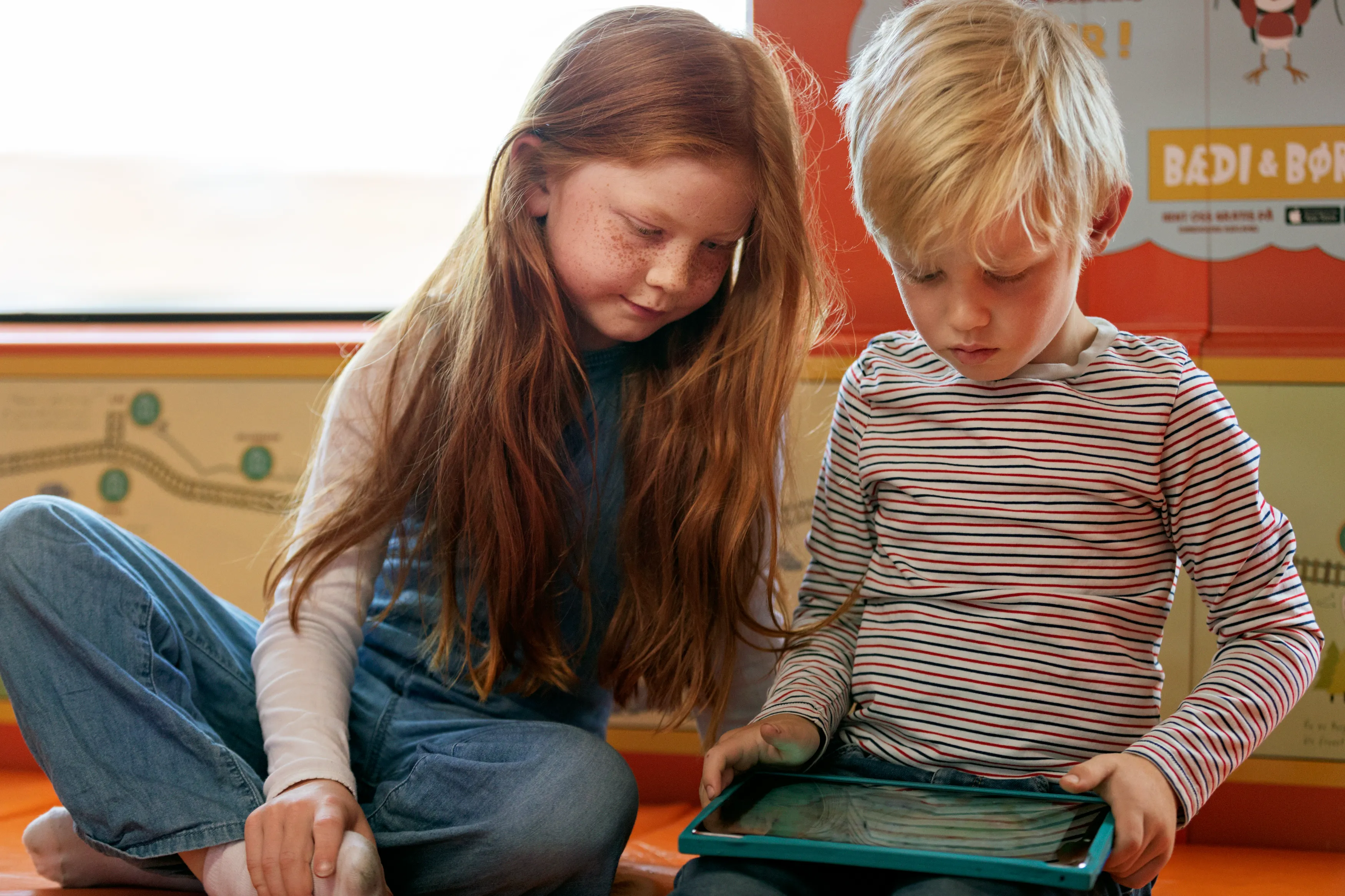 Gutt og jente sitter på gulvet i familievognen og ser på nettbrett