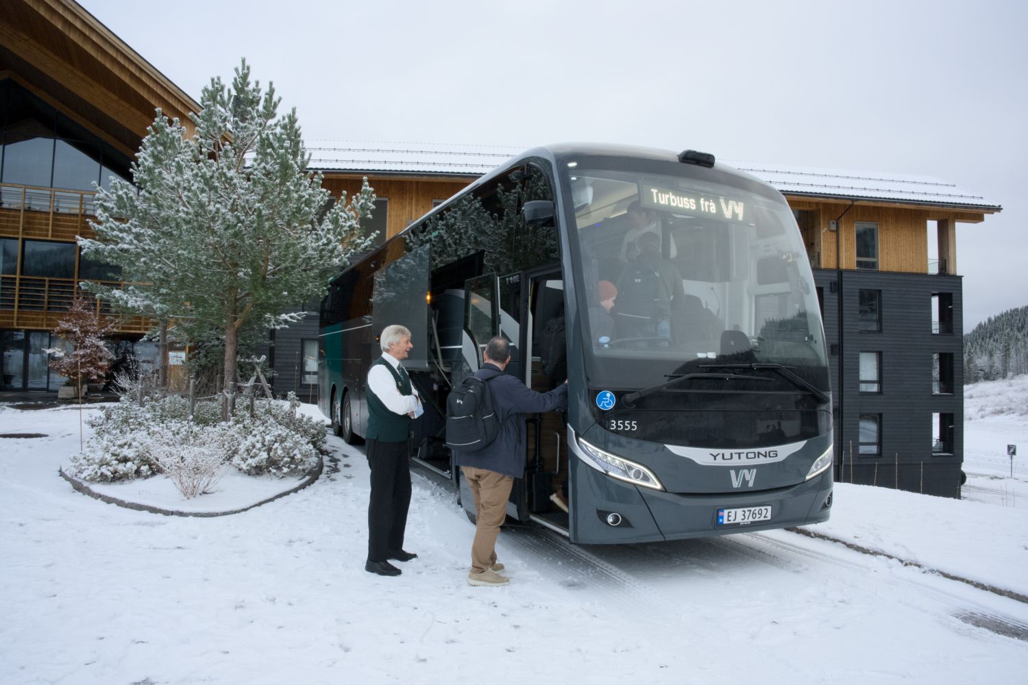 Vy-buss som står parkert utenfor et hotell og med folk på vei inn i bussen.