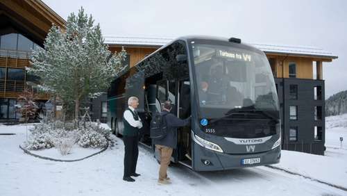 Vy-buss som står parkert utenfor et hotell og med folk på vei inn i bussen.