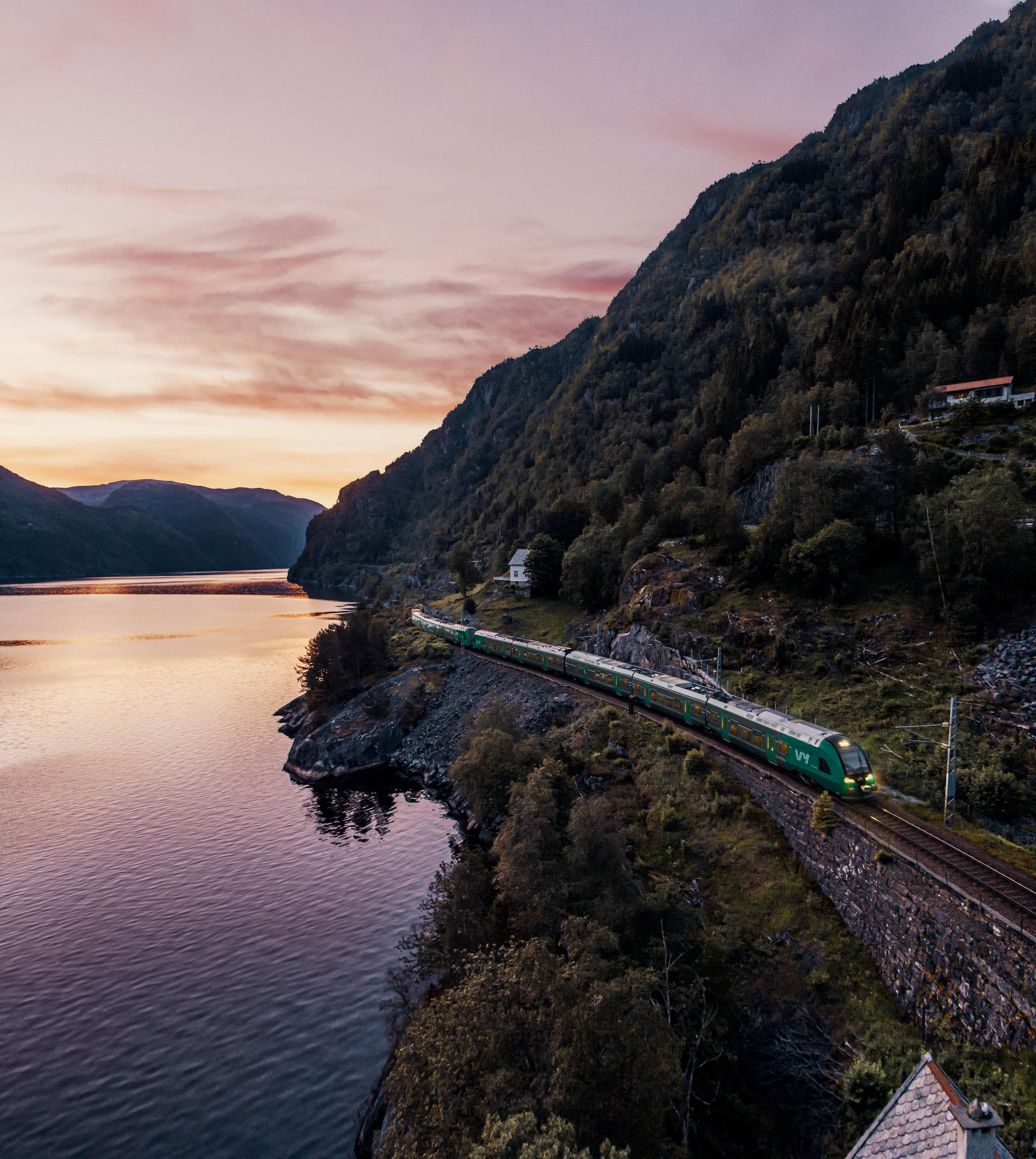 Toget kjører ved vannet ved Voss på Bergensbanen i solnedgang