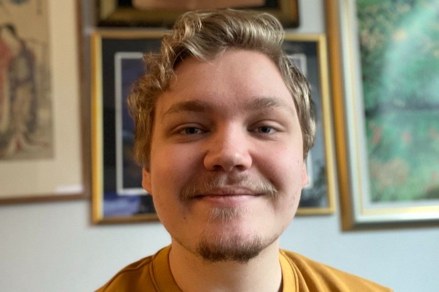 Bilde av Simen, i bakgrunnen henger det bilder på en vegg.