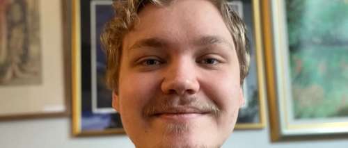 Bilde av Simen, i bakgrunnen henger det bilder på en vegg.