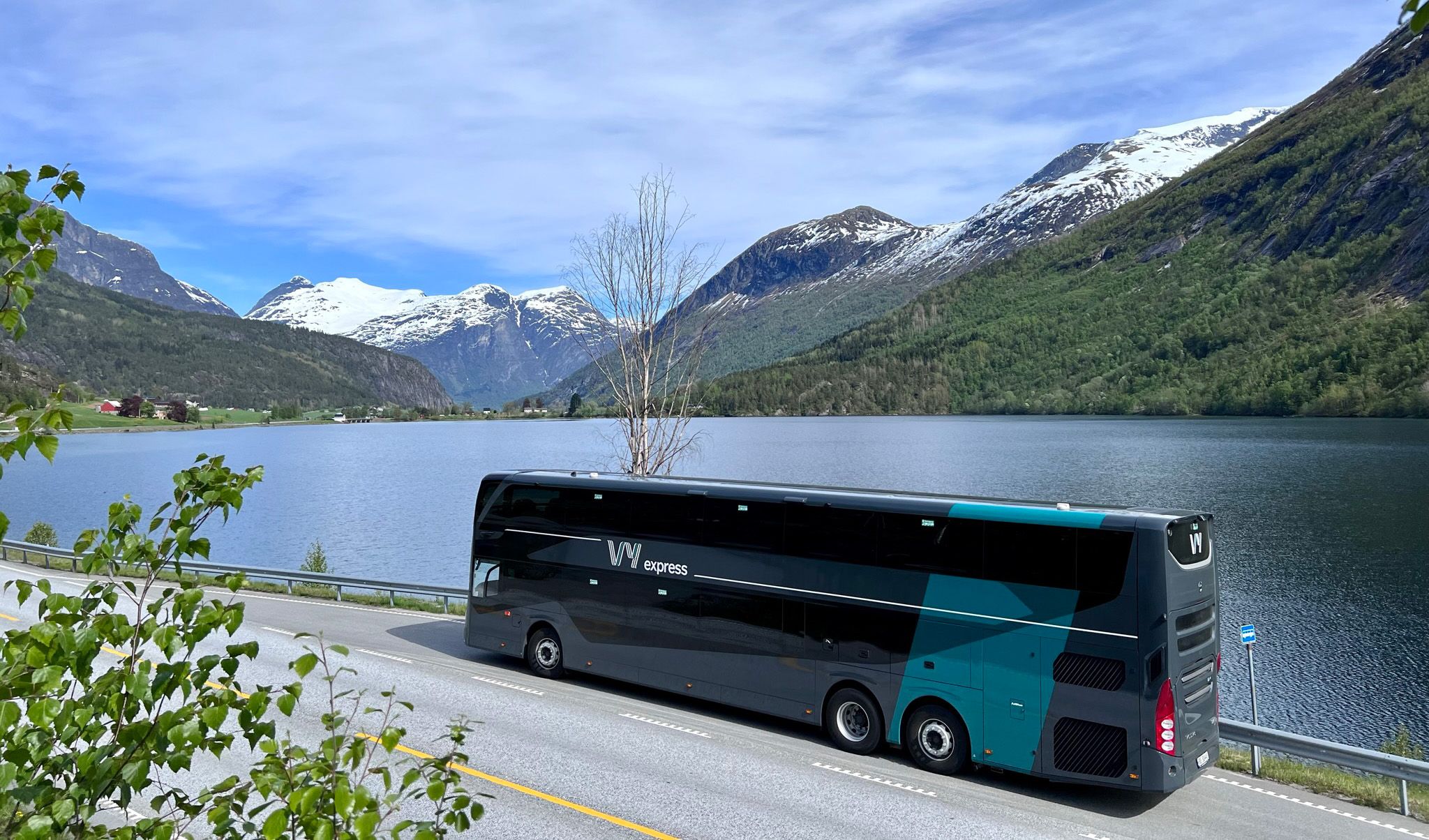 En Vy-buss som står parkert langs fjorden omringet av fjell.