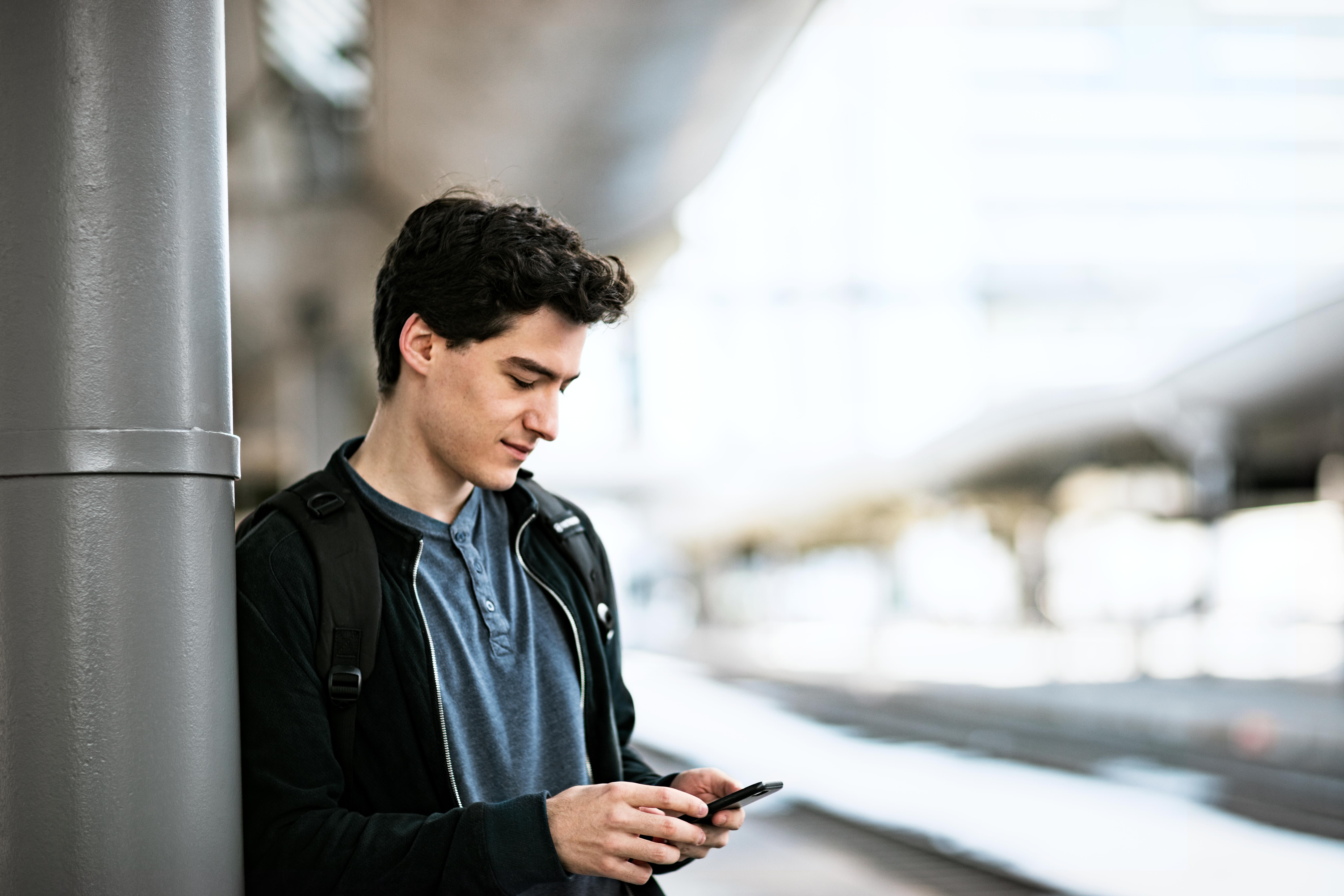 En ung mann ser på mobilen mens han venter på et tog på plattformen